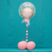 kleiner rosa Ballon in einem größeren durchsichtigen Ballon mit rosa Schleife und Schmetterlings-Deko